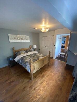 A bedroom with a wooden bed, a nightstand, a wall-mounted lamp, and a door leading to another room.