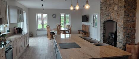 A modern kitchen with a large island, stone fireplace, and dining area with natural light.