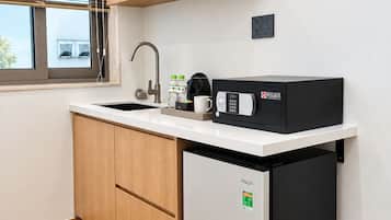 A compact kitchen with a built-in dishwasher, a microwave, a sink, and a window with blinds.