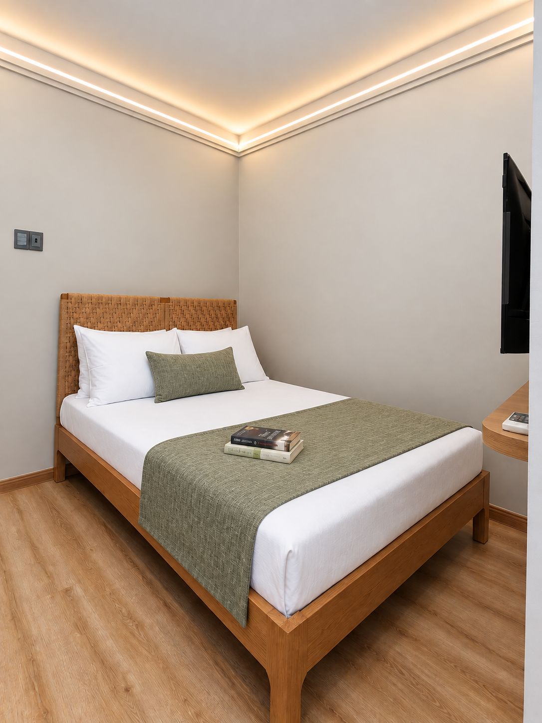 Een netjes opgemaakt bed met houten frame, witte beddengoed en een groene plaid.