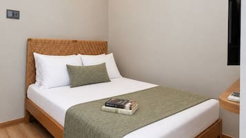 Een netjes opgemaakt bed met houten frame, witte beddengoed en een groene plaid.