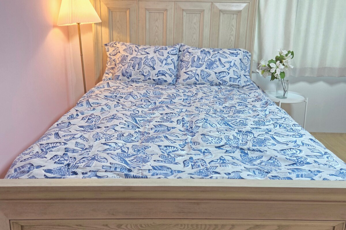 A bed with a patterned bedspread, a bedside lamp, and a vase with flowers on a bedside table.