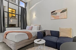 A bedroom with a bed, a sofa, a small round table, and a painting on the wall. - Modern CBD Studio with Kitchen near Sky Tower (Auckland CBD)
