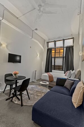 A modern living room with a sofa, a dining table with chairs, a TV, and a window with curtains. - Modern CBD Studio with Kitchen near Sky Tower (Auckland CBD)