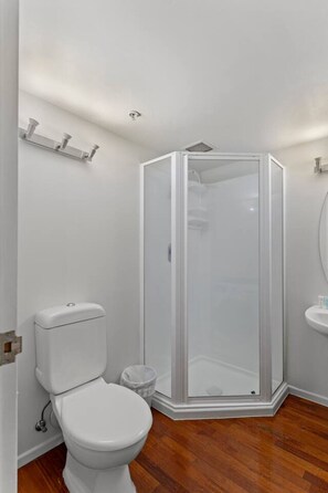 A corner bathroom with a toilet, a shower enclosure, and a sink. - Modern CBD Studio with Kitchen near Sky Tower (Auckland CBD)