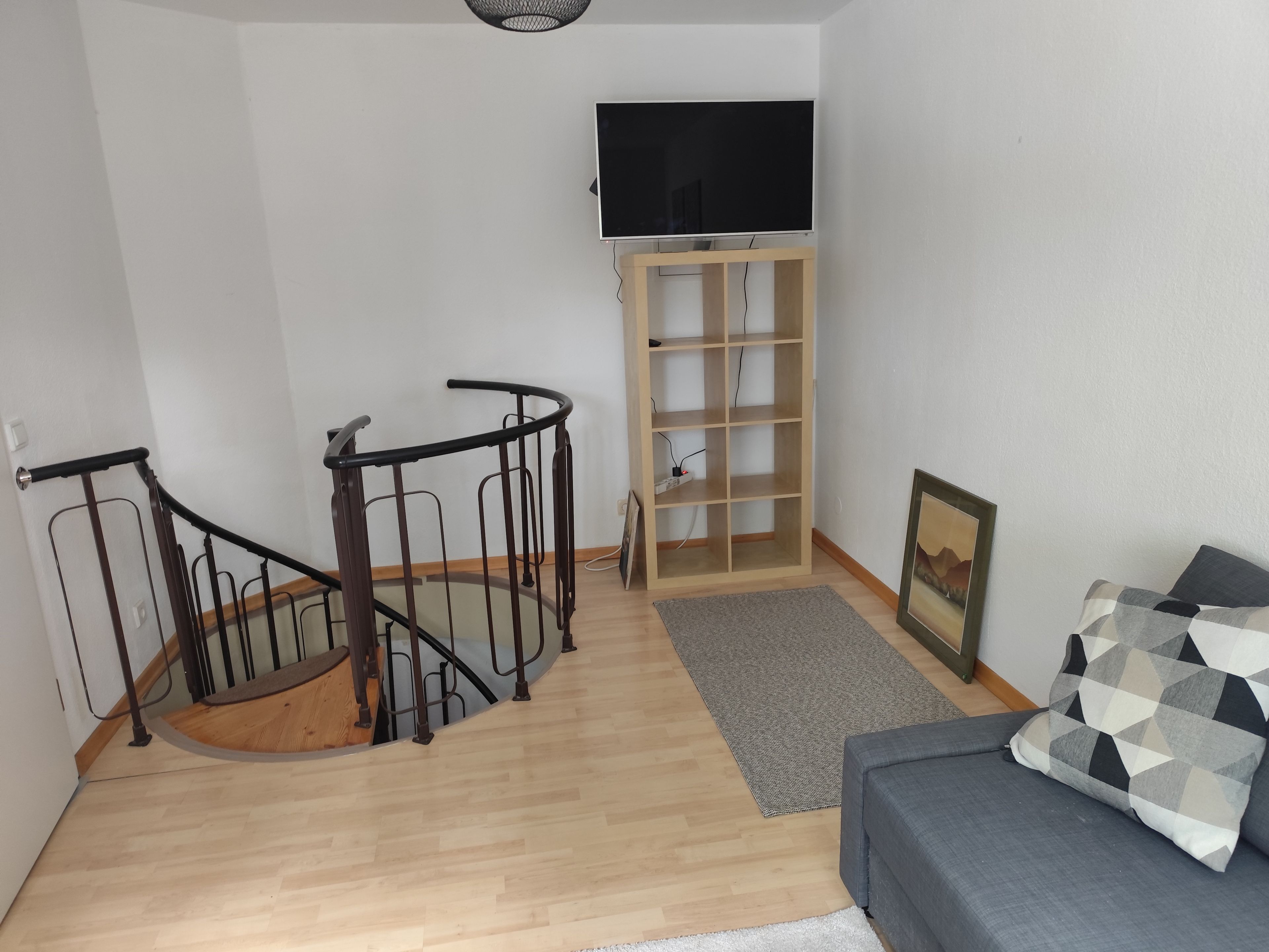 Ein Wohnzimmer mit Treppe, einem Flachbildfernseher, einer Holzkassette und einer Couch mit gemusterten Kissen.