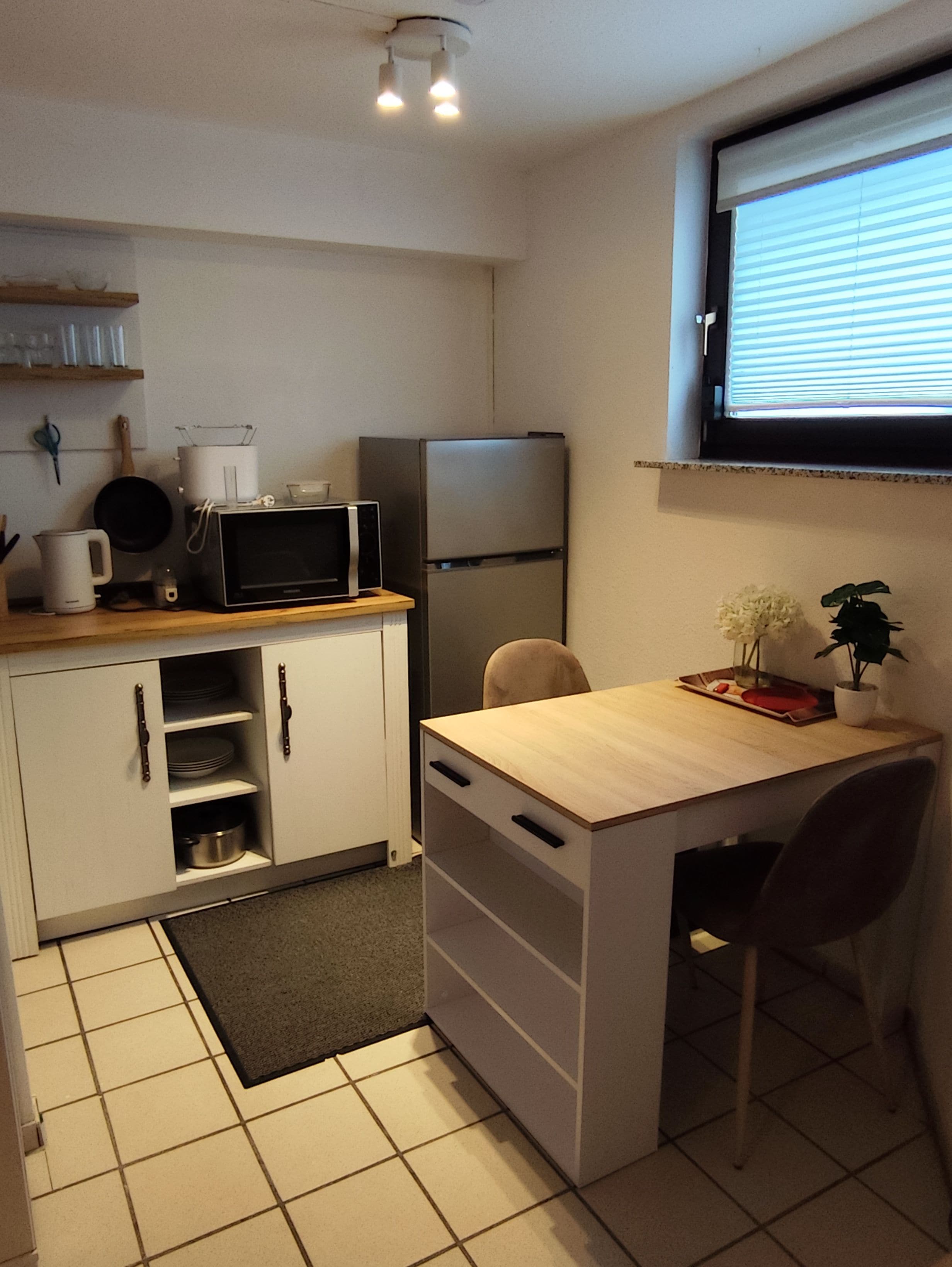 Eine kompakte Küche mit Mikrowelle, Kühlschrank und einem kleinen Esstisch mit Stühlen.