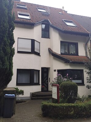 Ein zweistöckiges Gebäude mit einem Ziegeldach, mehreren Fenstern und einer Tür, die mit der Nummer 105 gekennzeichnet ist.