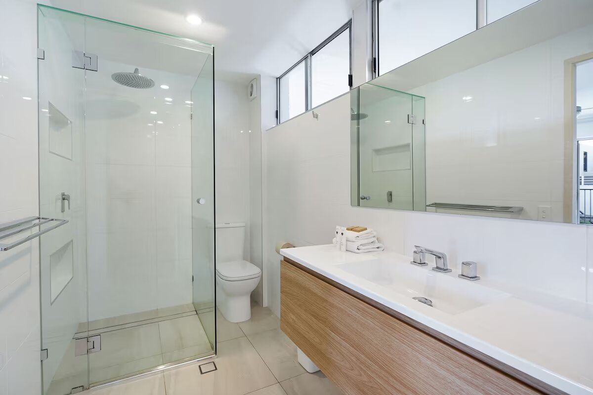 A modern bathroom with a glass shower enclosure, a toilet, a vanity with a mirror, and a sink.