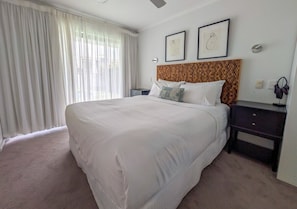 A hotel room with a large bed, a wooden headboard, a nightstand, a bedside table, and a window with curtains. - Couple Escape-10min walk to Hastings St&Beach (Noosa Heads)