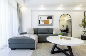 A modern living room with a grey sofa, a white coffee table, and a minimalist abstract painting. - 2BR Shangrila, Westlands Skyline Views-GTC&Sarit (Nairobi)