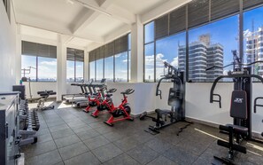 A gym with exercise equipment, large windows, and a view of a building under construction. - 2BR Shangrila, Westlands Skyline Views-GTC&Sarit (Nairobi)