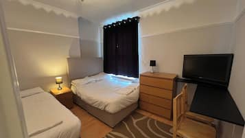 A hotel room with a bed, bedside table with lamp, dresser, desk with chair, and a television.