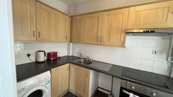 A kitchen with wooden cabinets, a washing machine, a stove, and a sink.