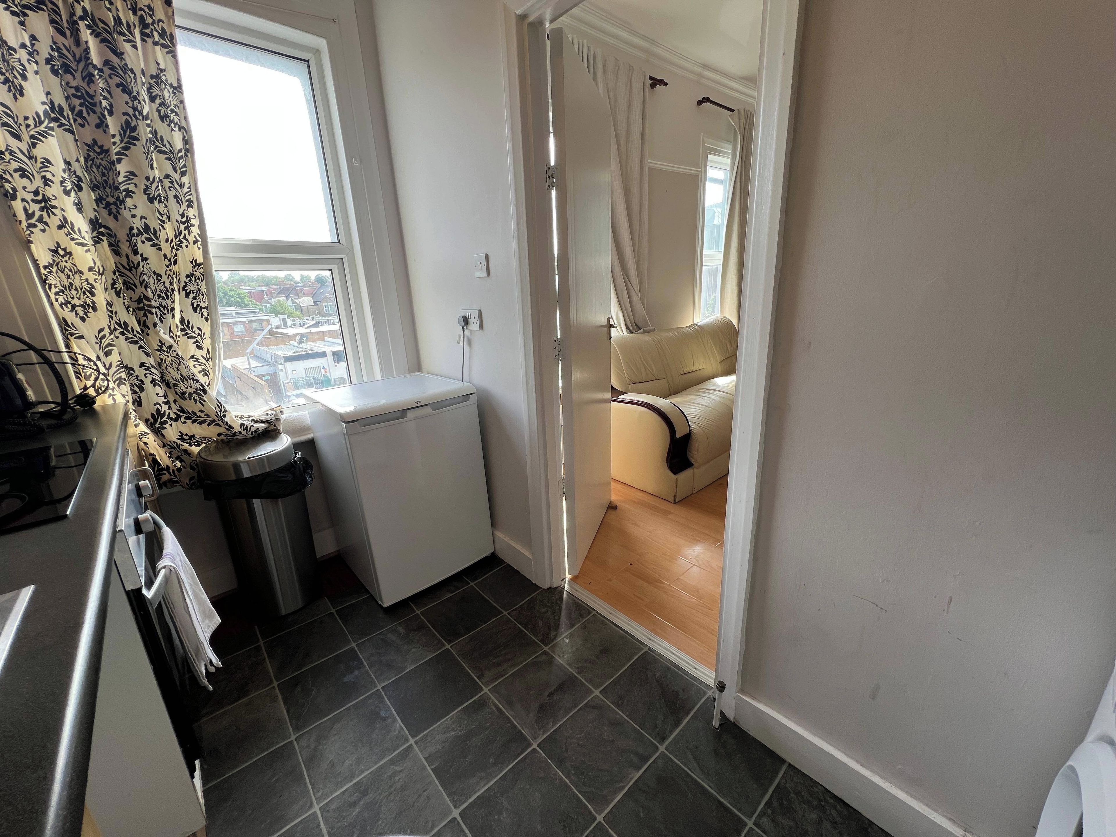 A compact kitchen with a refrigerator, a sink, and a window with patterned curtains.