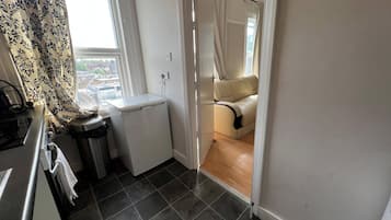 A compact kitchen with a refrigerator, a sink, and a window with patterned curtains.