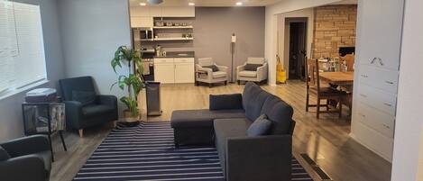 Ein modernes Wohnzimmer mit einer Couch, Sesseln, einem Streifenmuster-Teppich und einem Blumentopf.