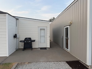 A compact outdoor area with a grill, a door, and a pathway leading to a building.