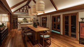 A spacious dining area with a wooden table and chairs, a kitchen in the background, and large windows with curtains. - Siritarar Residence by Elite Havens (Lipa Noi)