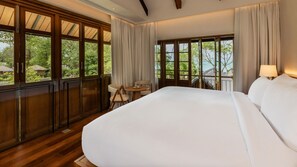 A large bed in a room with a view of greenery outside. There is a small table with chairs and a lamp. - Siritarar Residence by Elite Havens (Lipa Noi)