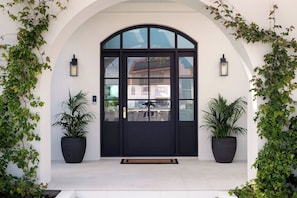 A black-framed entrance with a glass door, flanked by two potted plants, and a white arched doorway. - Isla by Khove - Mermaid Waters (Mermaid Waters)