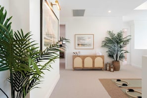 A hallway with a wooden cabinet, framed artwork, and potted plants. - Isla by Khove - Mermaid Waters (Mermaid Waters)