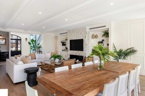 Un salon spacieux avec une grande table à manger en bois, des canapés blancs et une cheminée en pierre.