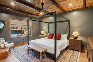 A four-poster bed with a wooden bench, a nightstand with a lamp, a wooden dresser, and a large window with a view. - 5-Bedroom Mountain Retreat • Fire Pit • Outdoor Wood-Burning Fireplace (McHenry)