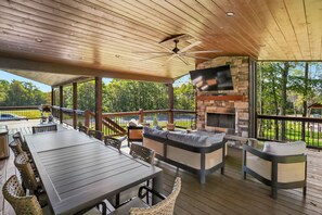 An outdoor deck with a stone fireplace, seating area, and a TV mounted on the wall. - 5-Bedroom Mountain Retreat • Fire Pit • Outdoor Wood-Burning Fireplace (McHenry)