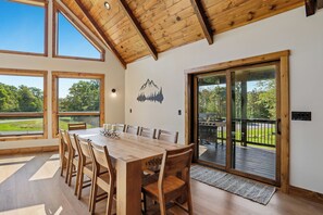 Un comedor con mesa y sillas de madera, ventanas amplias y vistas al exterior.