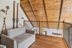 A wooden ceiling with a sloped design, a sofa, and a railing in a room with wooden flooring. - 5-Bedroom Mountain Retreat • Fire Pit • Outdoor Wood-Burning Fireplace (McHenry)