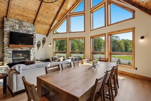Un espacio habitable amplio con chimenea de piedra, ventanas grandes y una mesa de comedor.