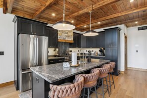 Een moderne keuken met een centraal eiland, roestvrijstalen apparatuur en een rustieke houten balkenplafond.