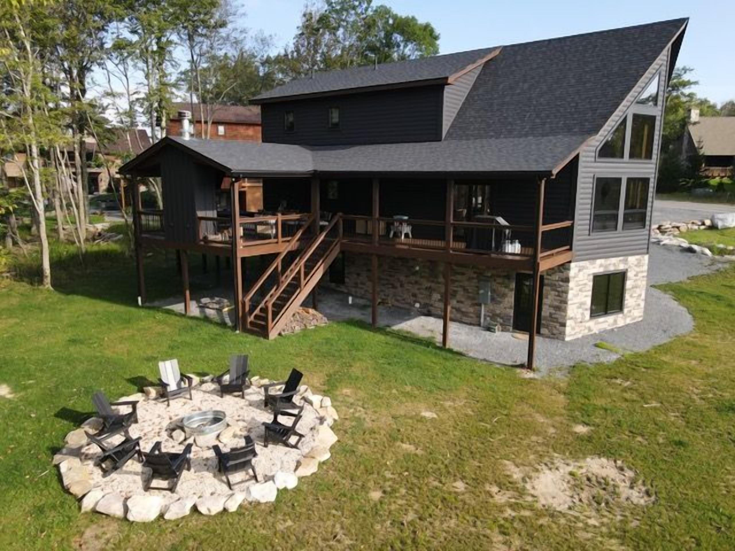 Ein modernes, zweistöckiges Haus mit Terrasse, Außenbereich mit Sitzgelegenheiten und einem Feuerkorb.