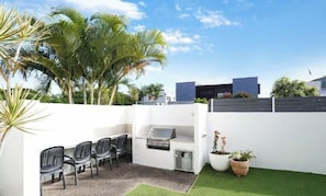An outdoor patio with a grill, seating, and potted plants. - Ocean Breeze Haven 1 Bed Apartment (Noosa Heads)