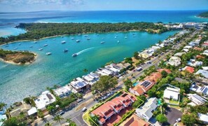 An aerial view of a coastal town with a marina, residential buildings, and a road. - Ocean Breeze Haven 1 Bed Apartment (Noosa Heads)