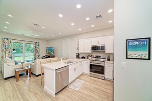Una cocina moderna con armarios blancos, electrodomésticos de acero inoxidable y un comedor con una mesa y sillas blancas.