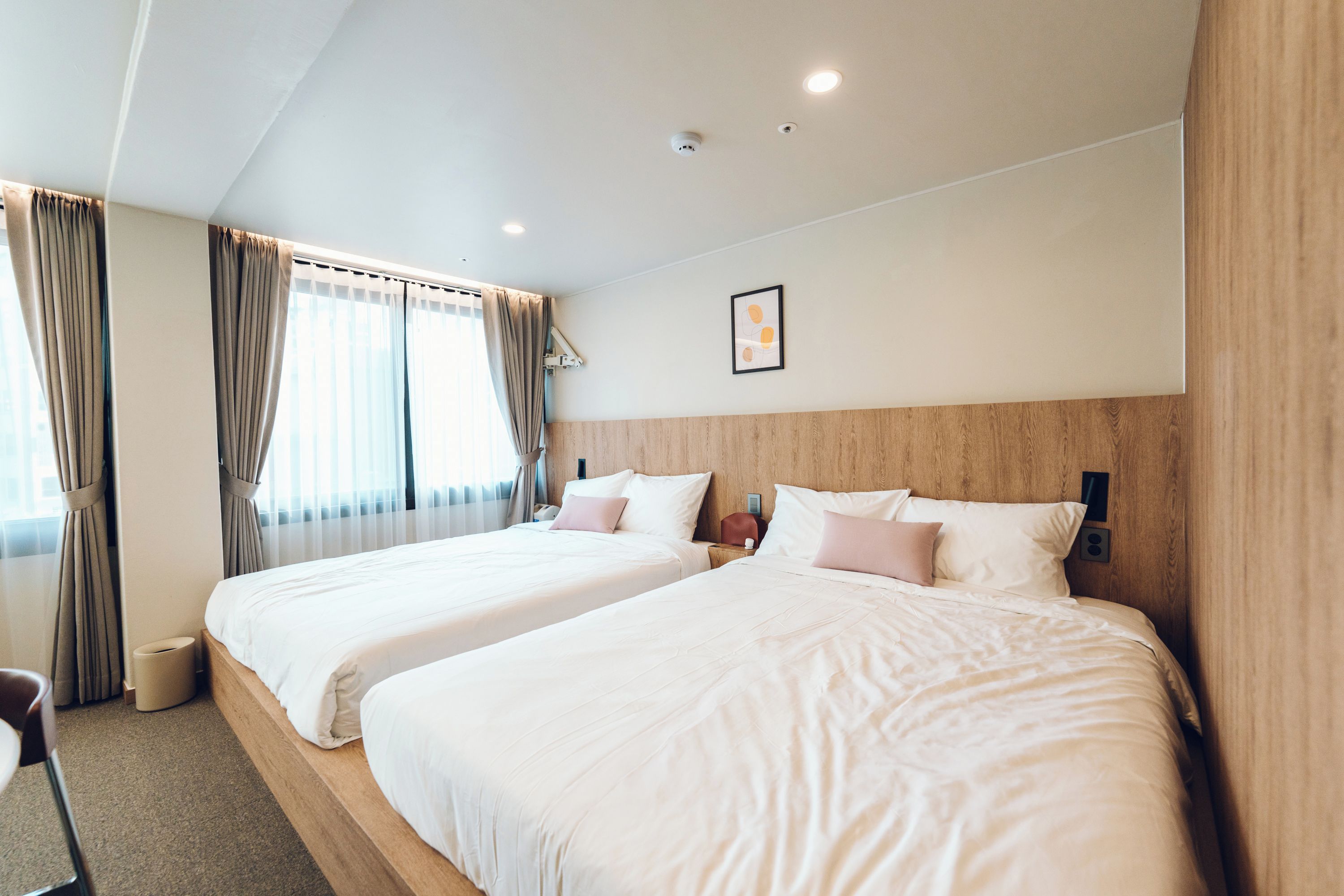 Une chambre d’hôtel avec deux lits, une tête de lit en bois, une table de chevet, une commode, une lampe et une fenêtre avec des rideaux.