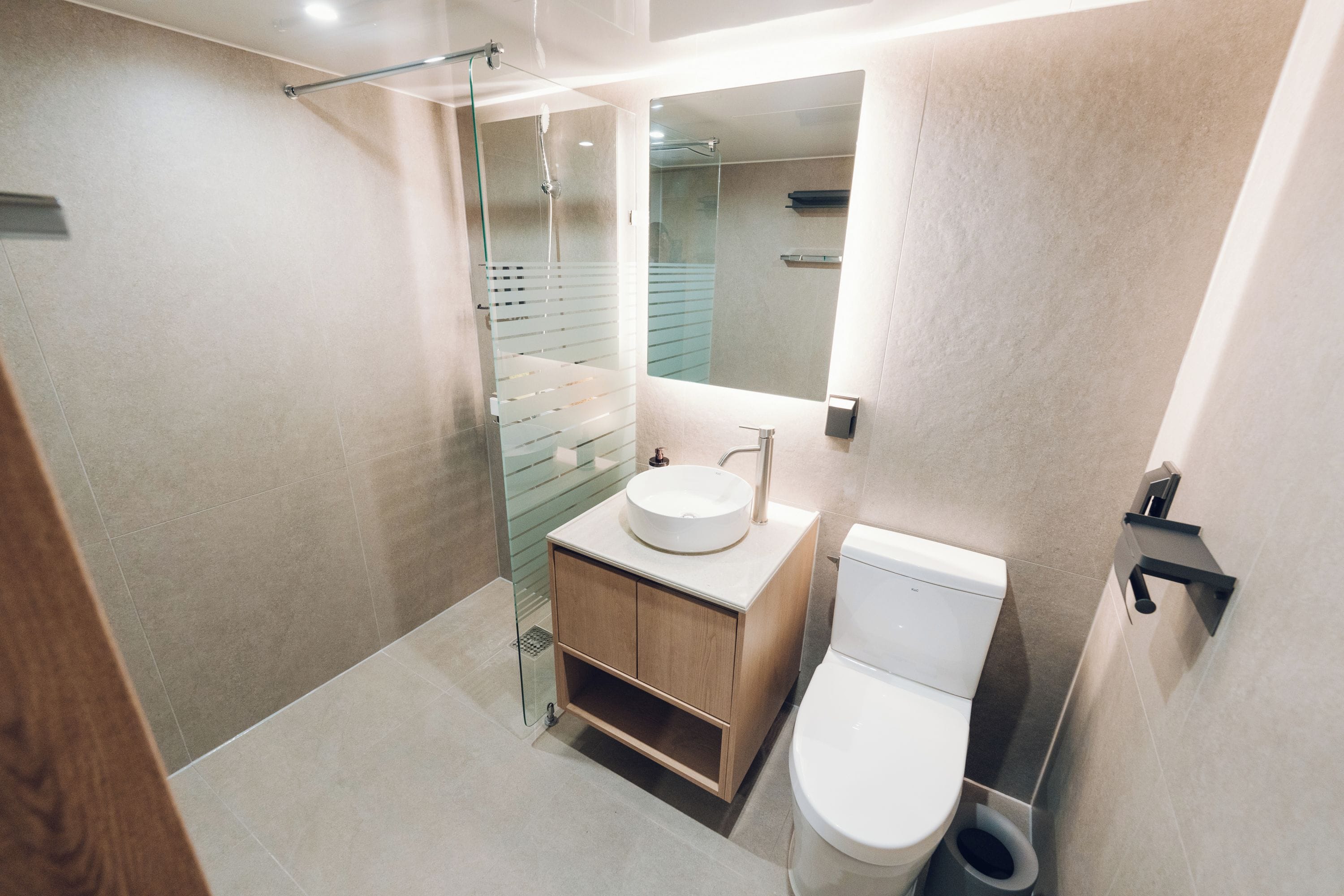 A modern bathroom with a glass shower enclosure, a wooden vanity with a white sink, and a white toilet.