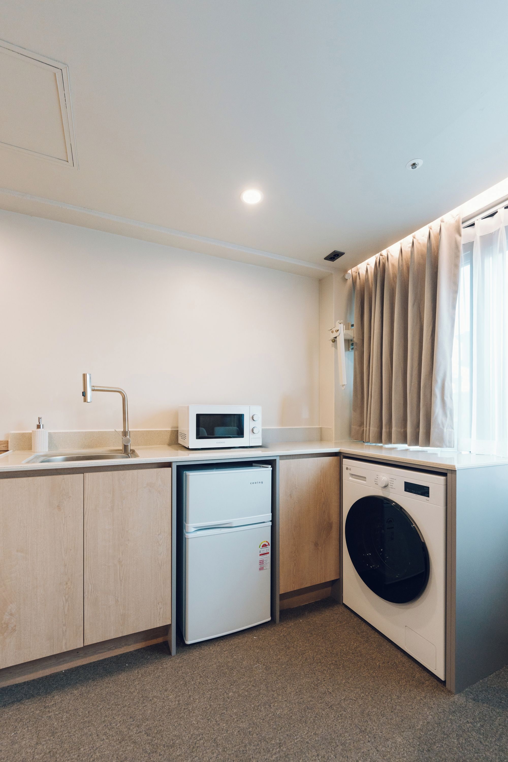 Une cuisine compacte équipée d’un four à micro-ondes, d’un mini-réfrigérateur, d’un lave-linge et d’un évier.