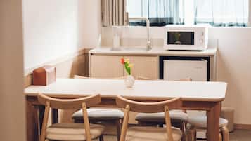 A compact hotel room with a kitchenette, a dining table with chairs, and a small white vase with flowers.