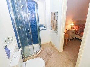 A bathroom with a glass shower enclosure, a toilet, a sink, a towel rack, and a bedside table with a lamp. - Tall Ships Lower Ground Apartment (Tenby)