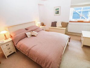 A bedroom with a bed, bedside tables, a nightstand, a dresser, a window with a view, and a painting on the wall. - Tall Ships Lower Ground Apartment (Tenby)