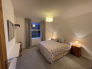 Ein Schlafzimmer mit einem Bett, Nachttischlampen, einem Fenster mit Vorhängen, einer Heizung und einer Tür.