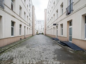 Une ruelle étroite, située entre deux bâtiments, avec un trottoir pavé, une petite rampe et un panneau indiquant un salon de manucure.