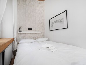 A neatly made bed with white linens, a white shelf with a lamp, and a framed picture on the wall. - Narutowicza 41 Boutique Apartment #2 (Łódź)