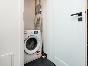 Une petite buanderie équipée d’un lave-linge à chargement frontal, d’un étendoir et d’une porte dotée d’une poignée noire.