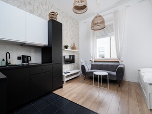 A modern kitchen with black cabinets, a black countertop, and a black floor mat. There is a grey sofa and a small white table in the living area. - Narutowicza 41 Boutique Apartment #2 (Łódź)