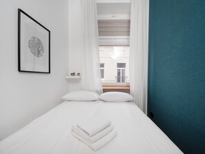 Une chambre d’hôtel avec un lit, un tableau encadré au mur, une fenêtre avec des rideaux et une vue sur les bâtiments à l’extérieur.
