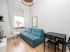Een moderne woonkamer met een blauwgroene bank, een klein rond tafeltje, een zwarte eettafel met stoelen, een rieten plafondlamp en een ingelijst schilderij aan de muur.